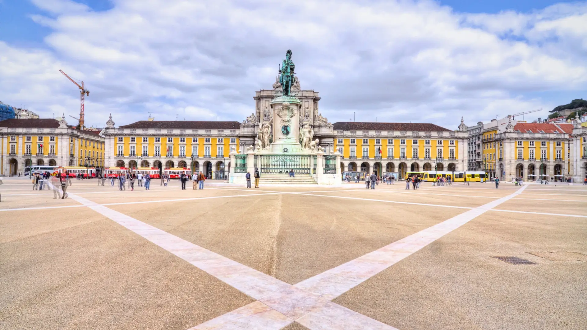 Wide view across the open paved square of Praça do Comércio showing the King José I equestrian statue and yellow arcaded buildings in Lisbon.