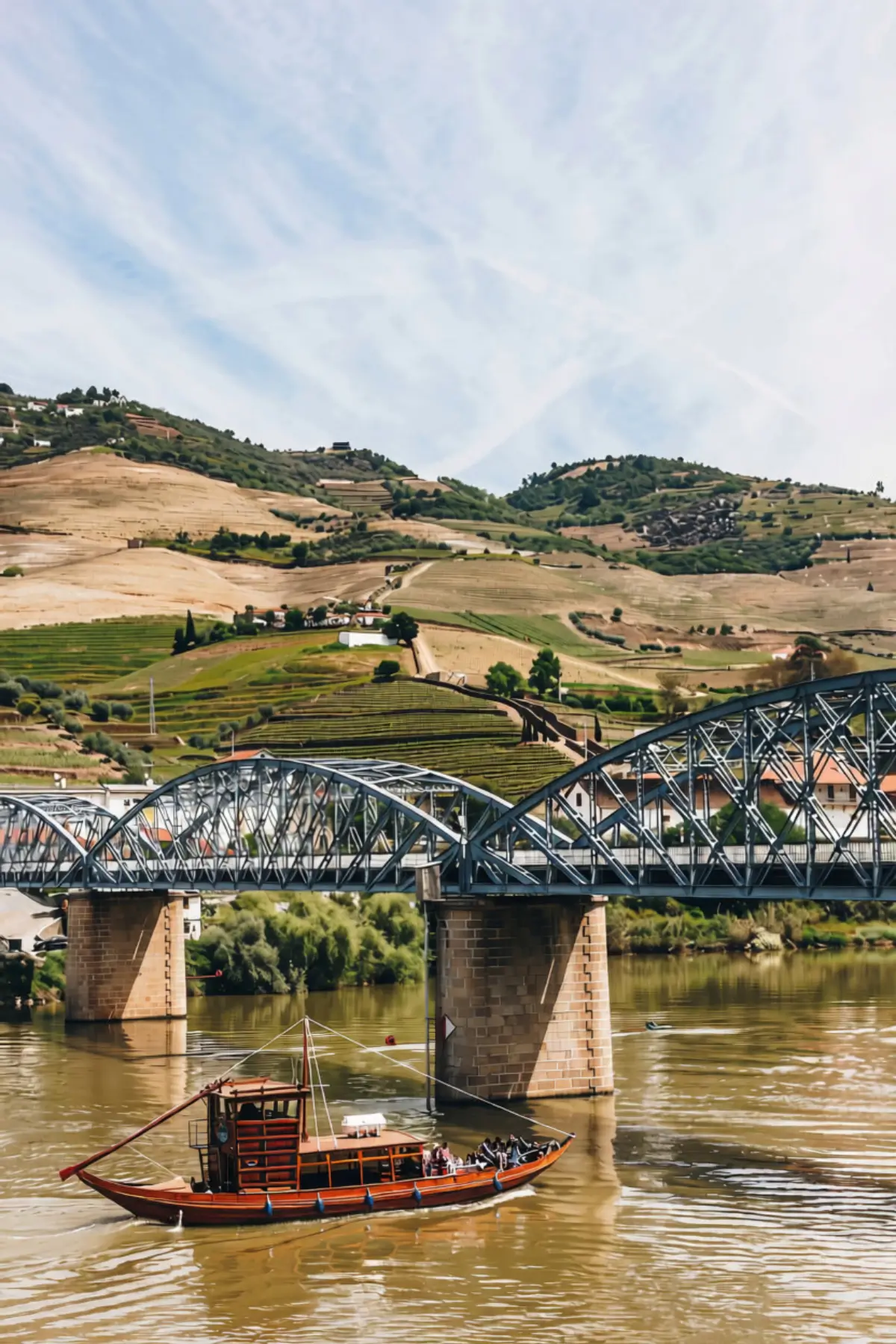 Metal bridge over the Pinhão River with terraced vineyard slopes behind it.
