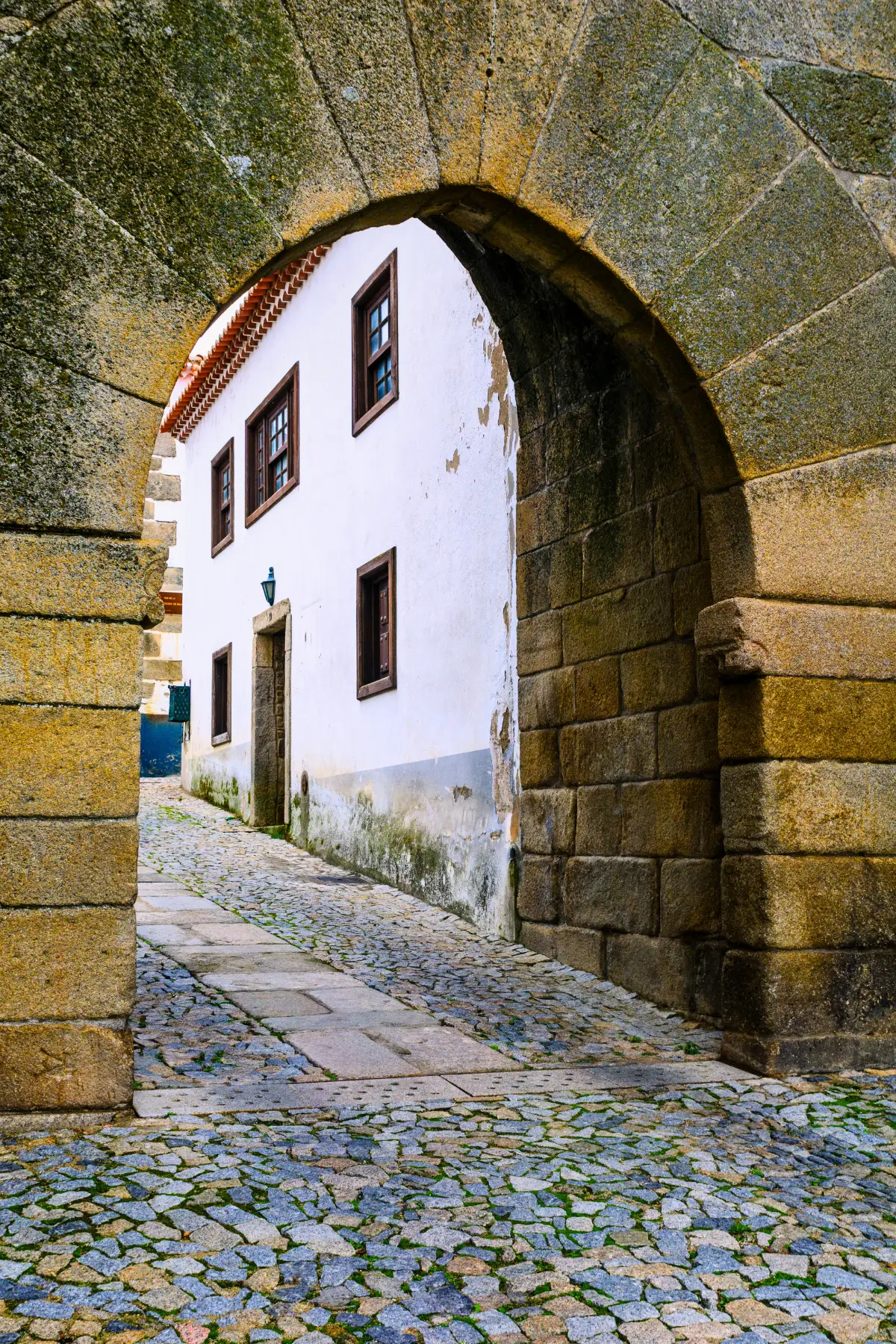Old stone arch framing a cobbled street and traditional white building in northern Portugal.