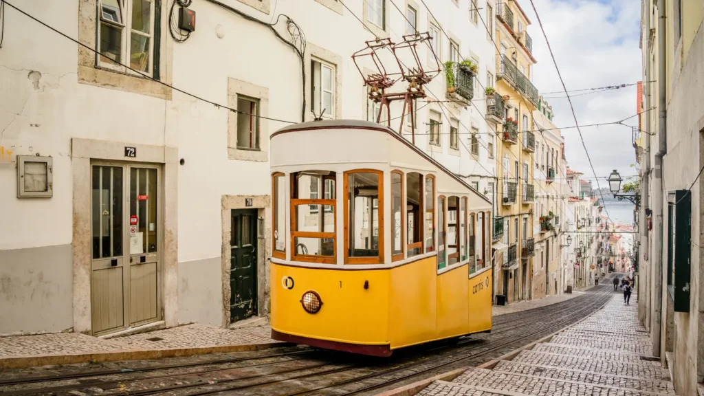 Yellow Tram 28 travelling along a steep street in Lisbon.