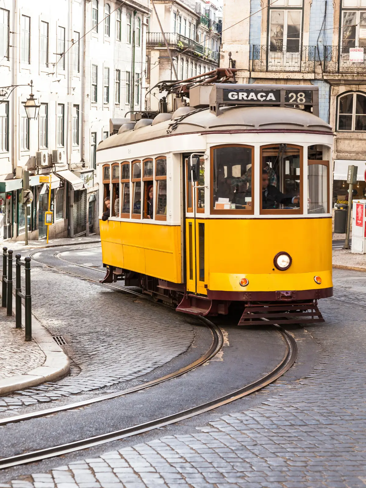 Iconic yellow Tram 28 navigating a curved cobblestone street past traditional buildings in Lisbon.