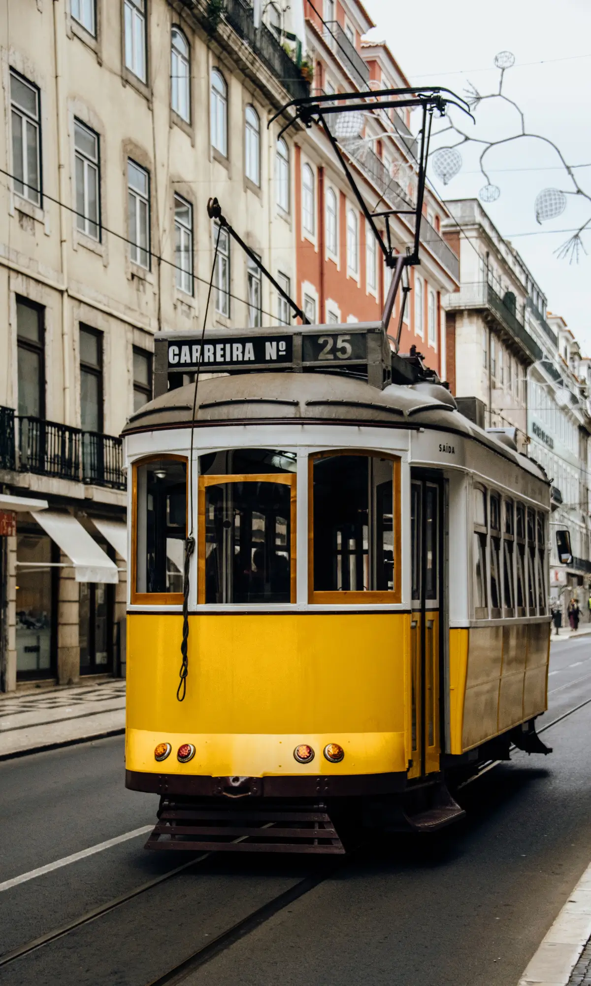 Yellow Lisbon tram travelling along a city street.