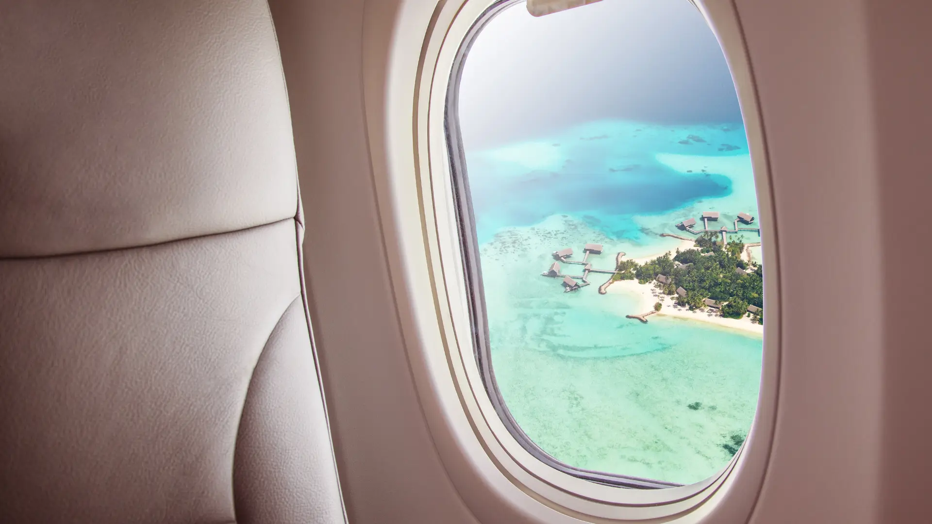 Airplane window overlooking a tropical island and turquoise water.