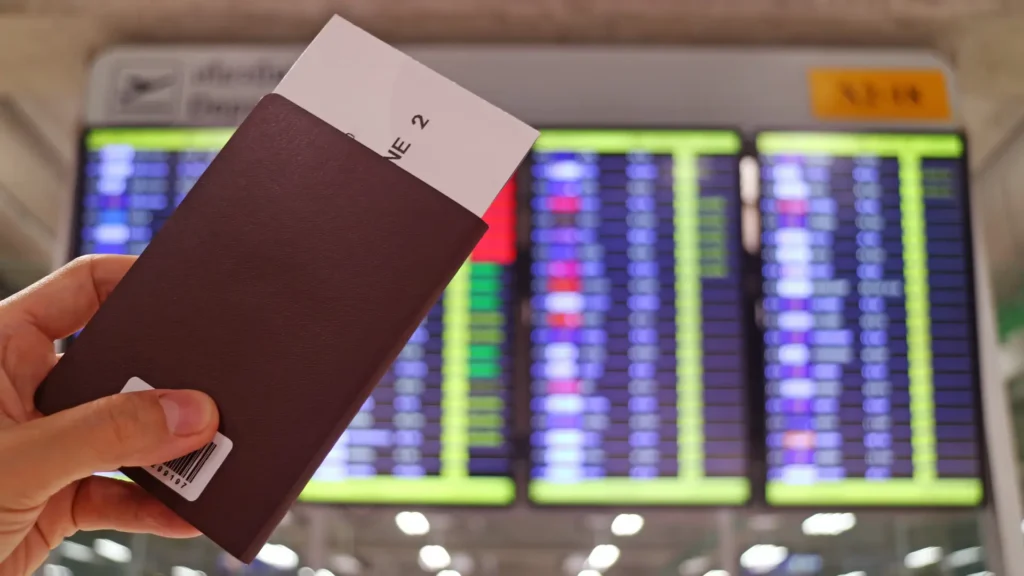 Passport and boarding pass in front of airport departure boards.
