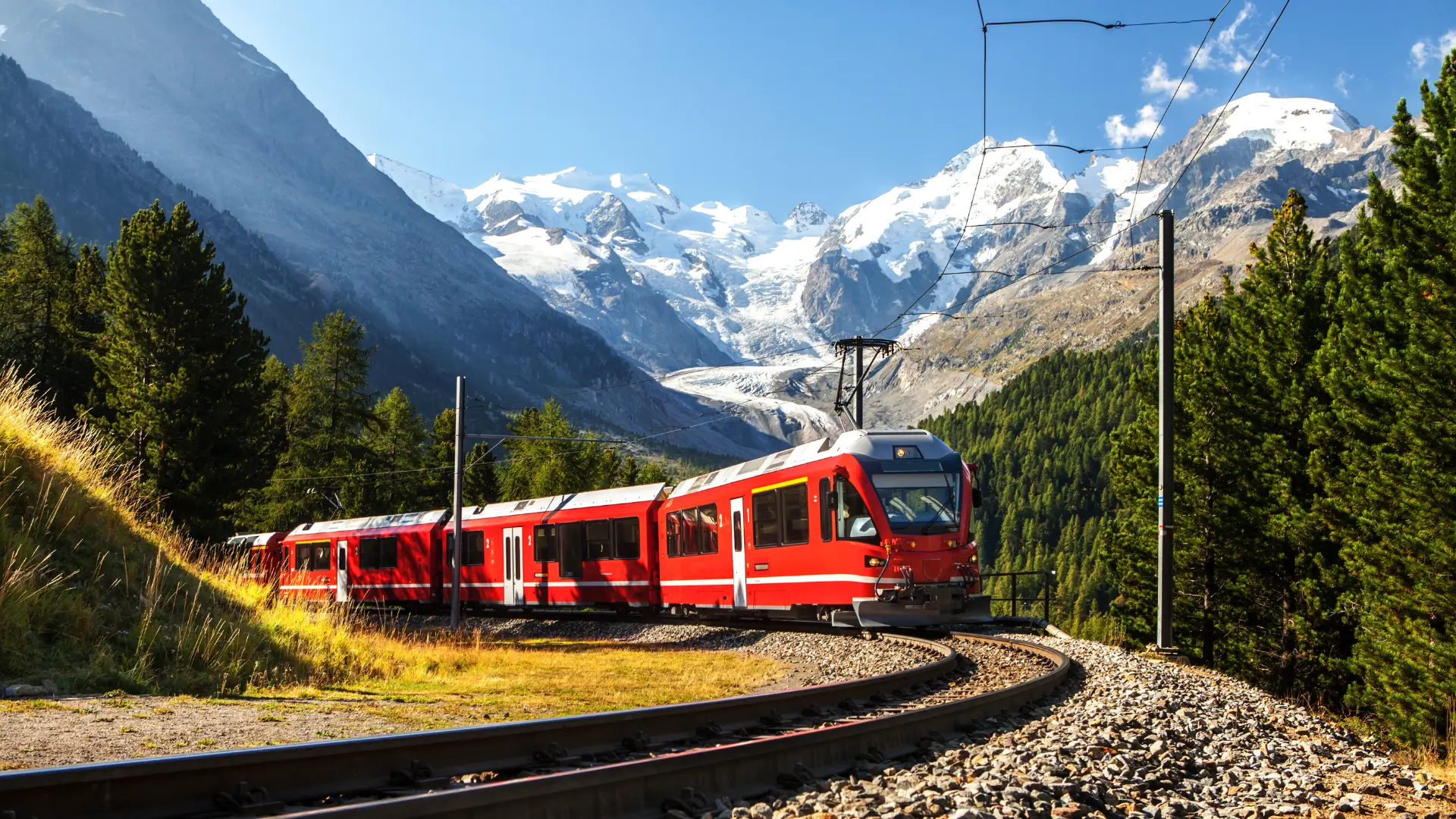 Red train travelling through the Swiss Alps with snow-covered mountains in the background.